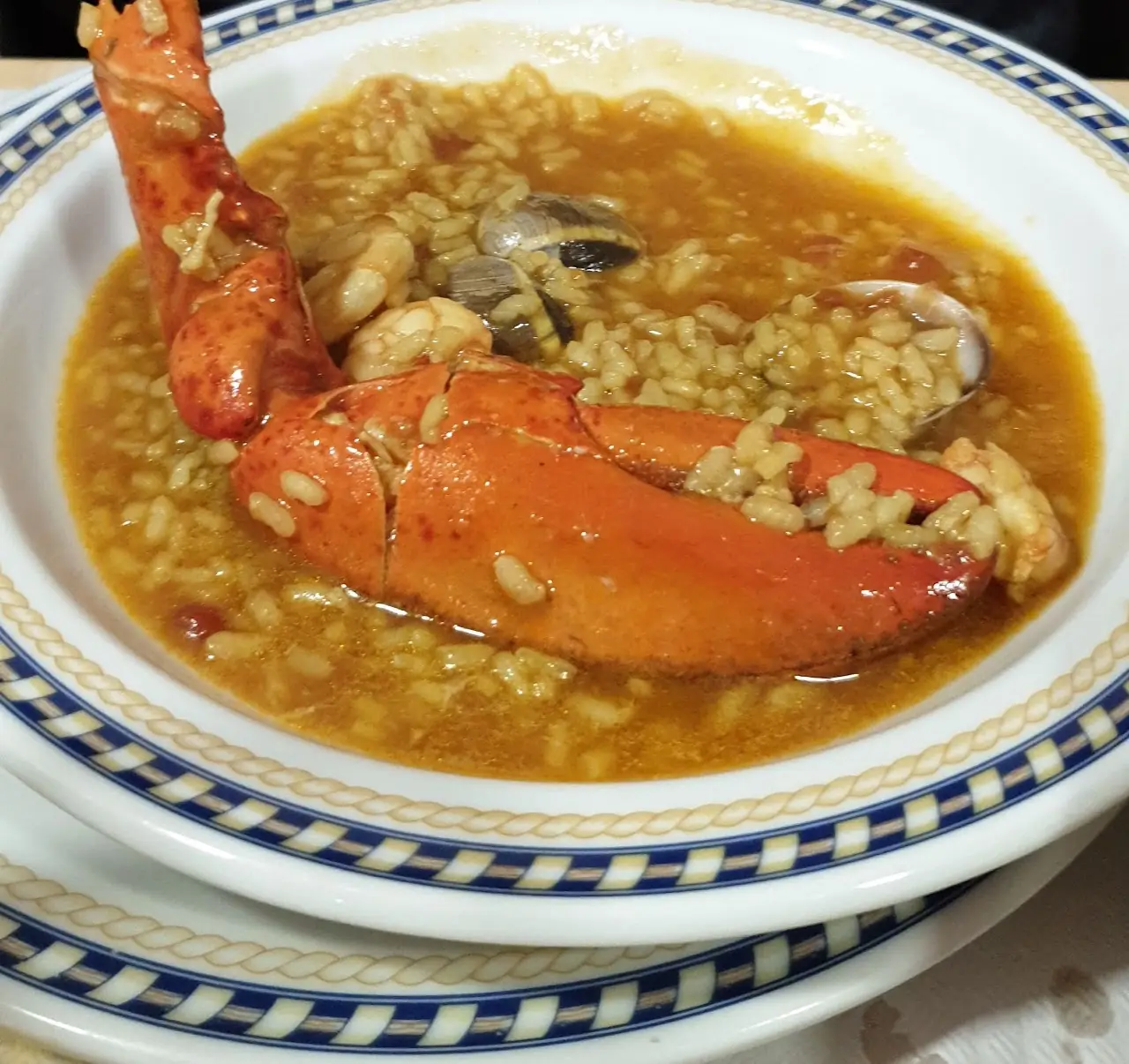 Soupy rice with half a lobster and clams in a white bowl with a blue patterned rim