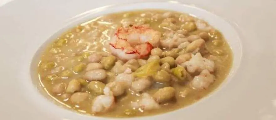 White bowl of white bean and pea stew topped with shrimp, Arturo