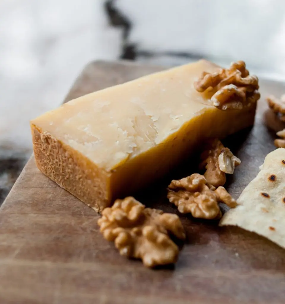 Wedge of aged cheese with walnut halves and a crisp cracker on a wooden board