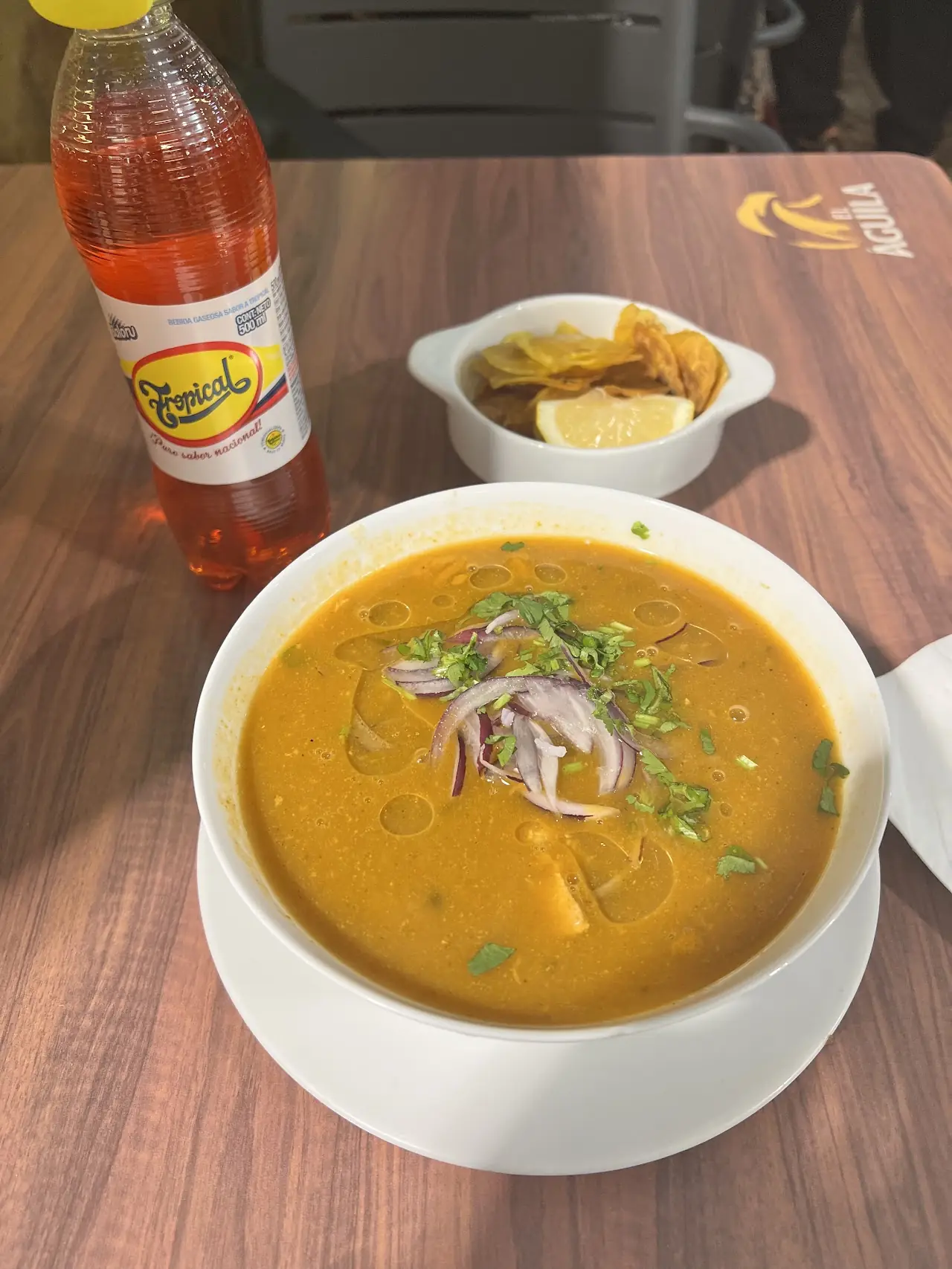 A bowl of orange fish soup topped with red onion and herbs, with a side of crisp plantain chips