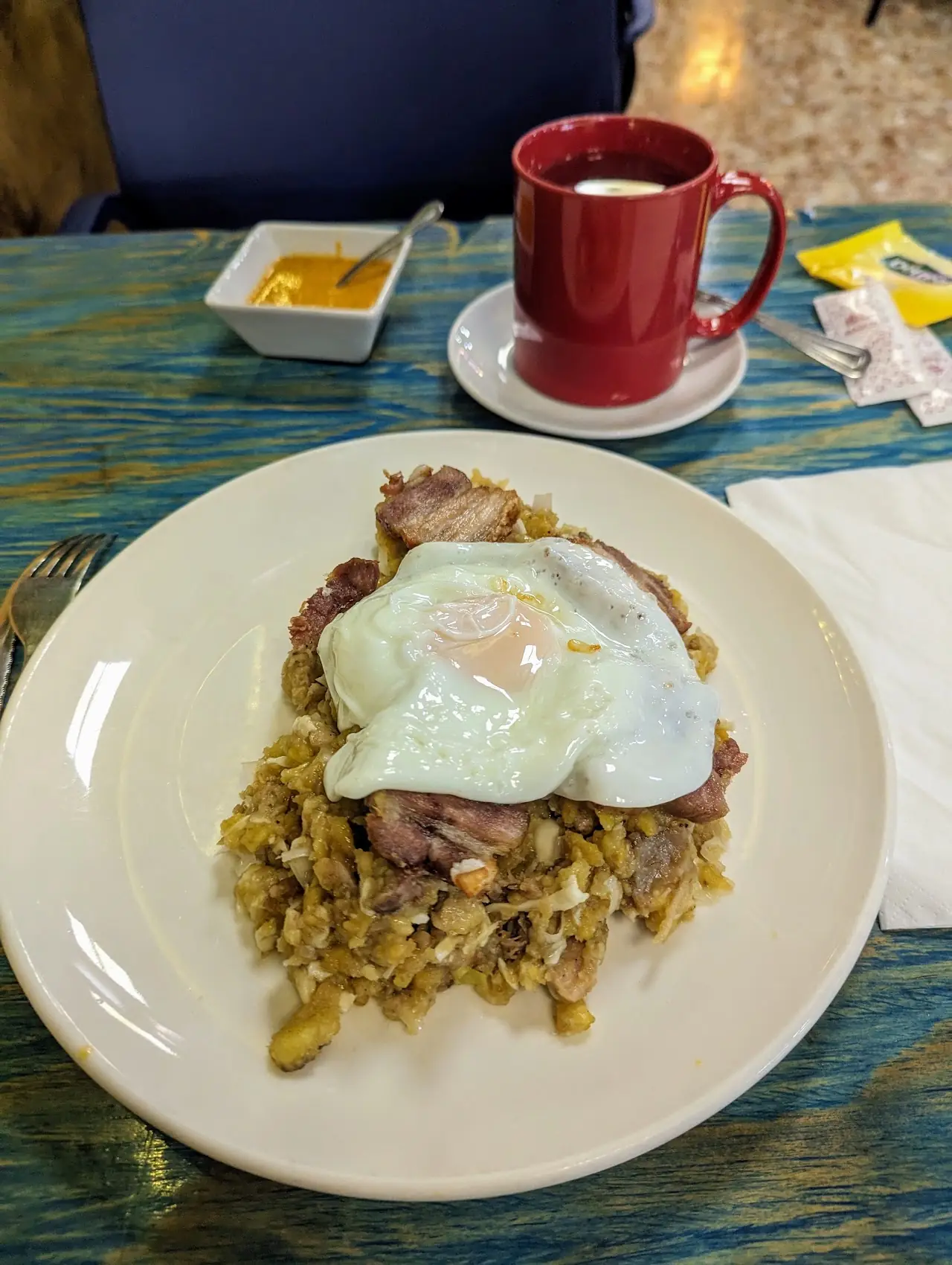 A fried egg over grilled meat and toasted corn, with a red mug of coffee