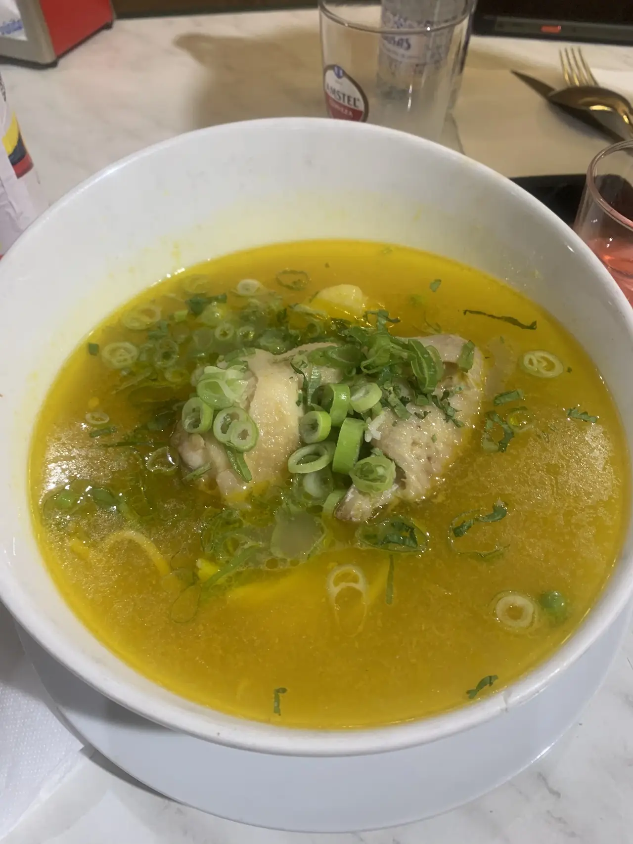 A clear chicken broth with potato and spring onion in a white bowl