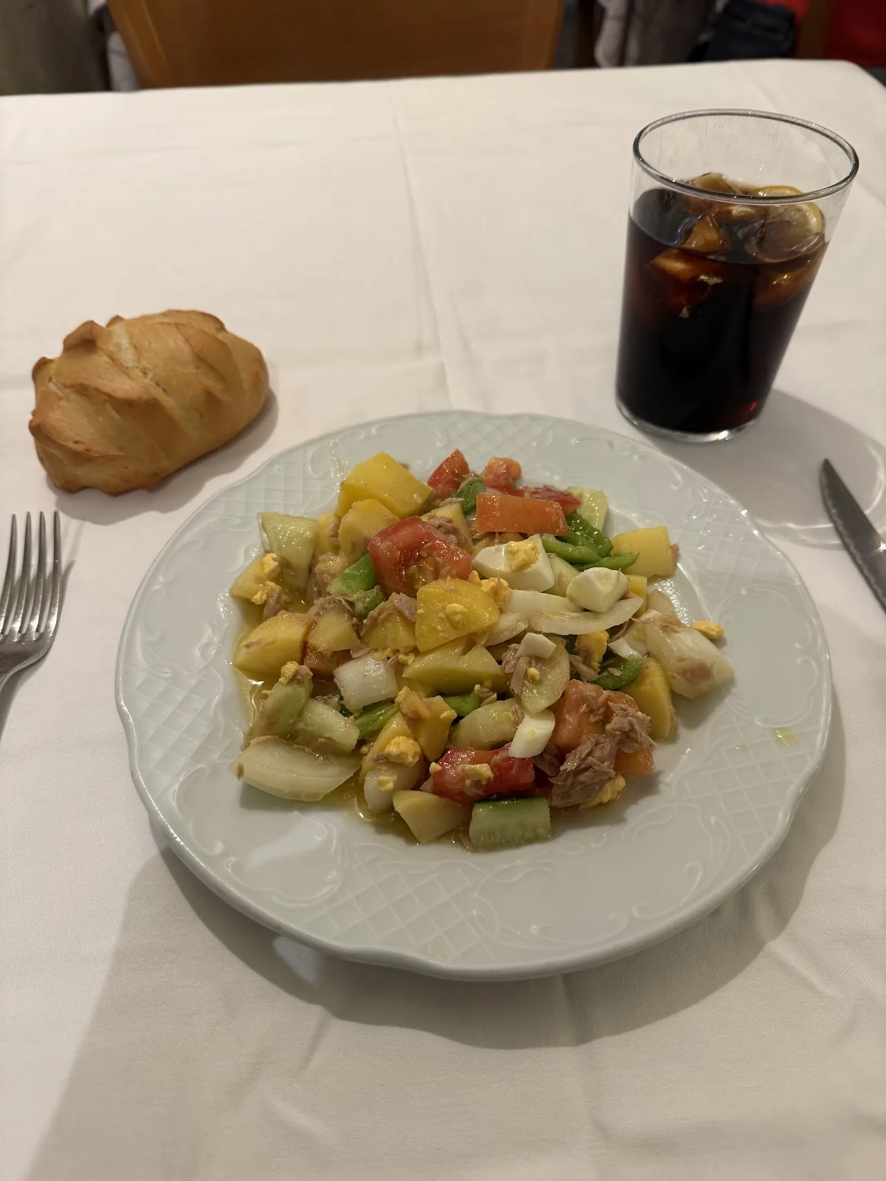 A plate of vegetable and potato salad with bread and a cola