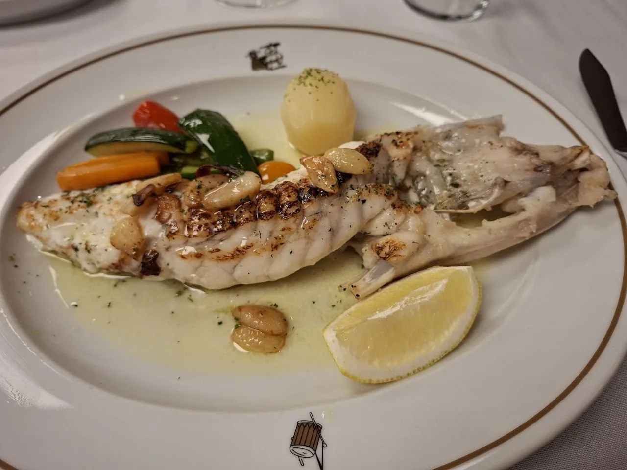 A whole grilled fish served with vegetables and a lemon wedge
