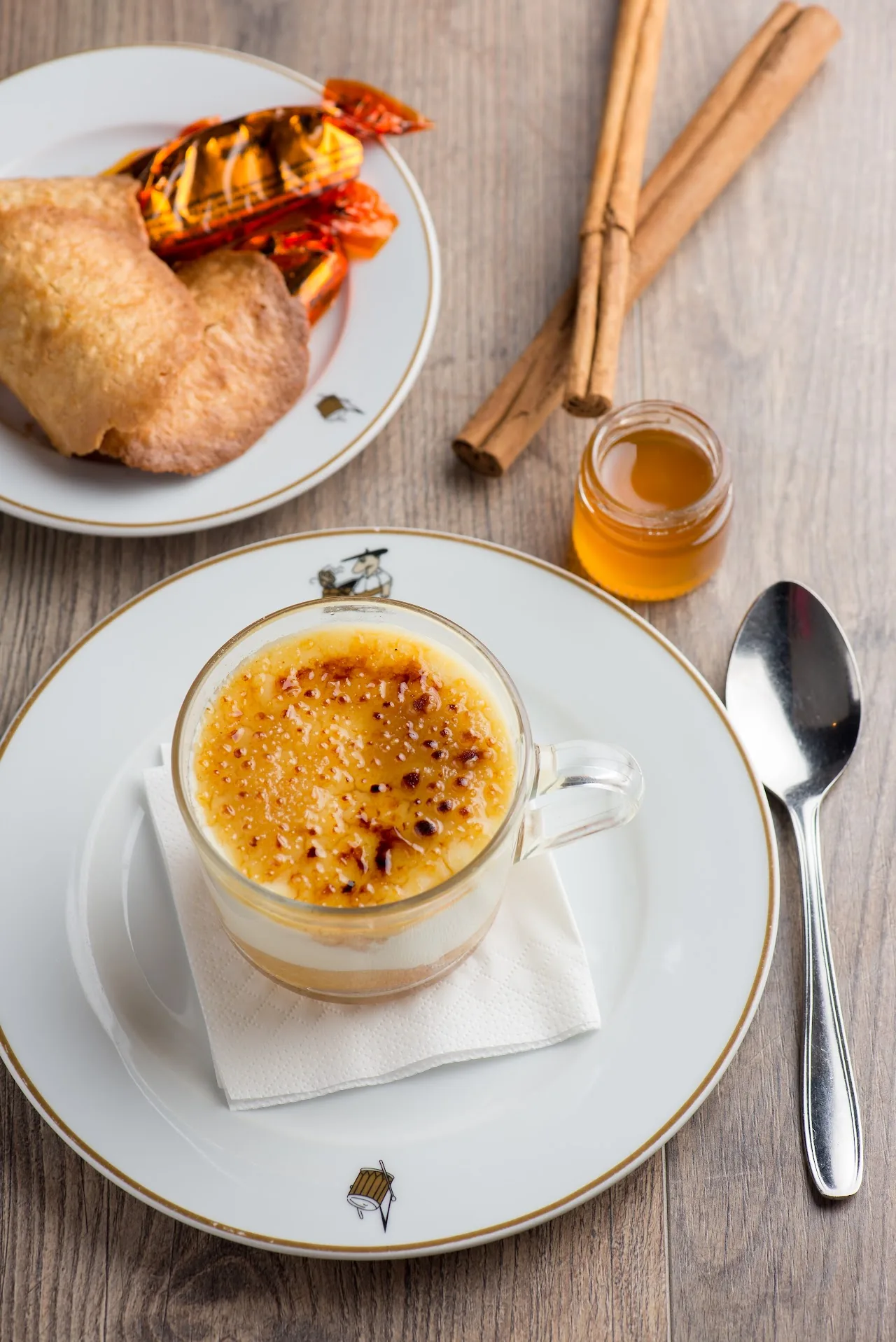 A crème brûlée dessert with a pastry and cinnamon sticks on the side