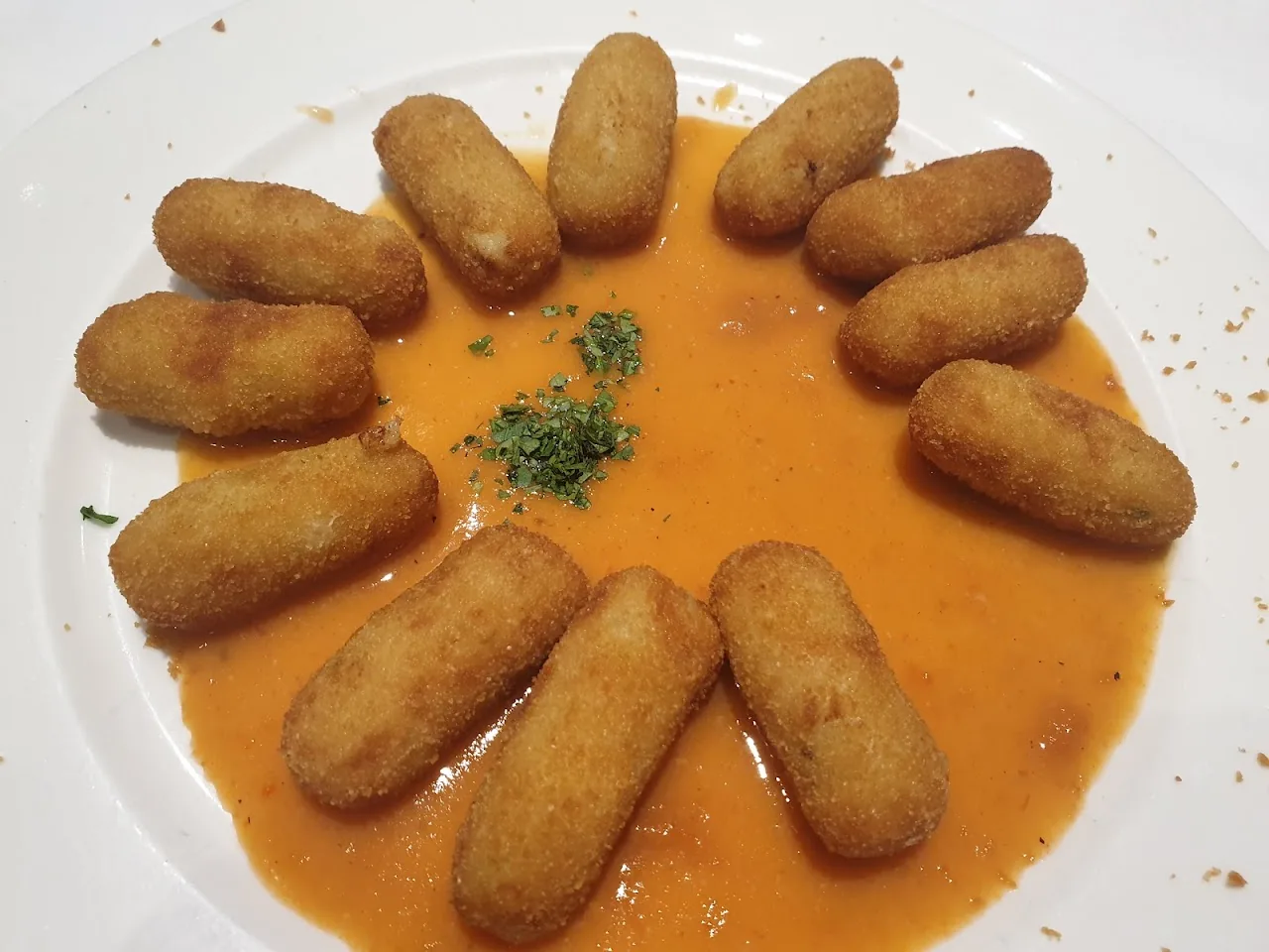 A ring of golden croquettes on a plate with red sauce