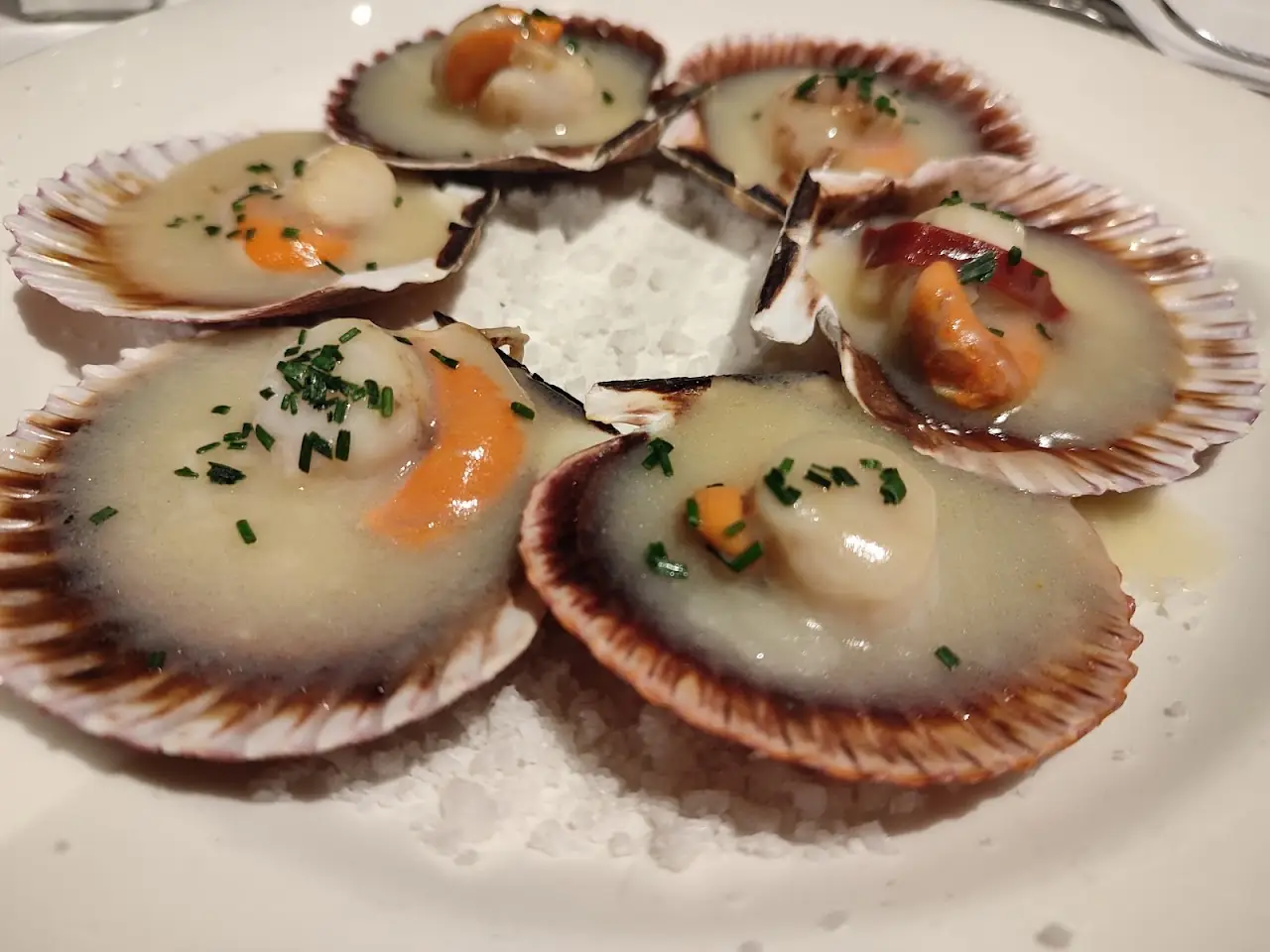 Scallops on the half shell with a citrus garnish, plated on ice.