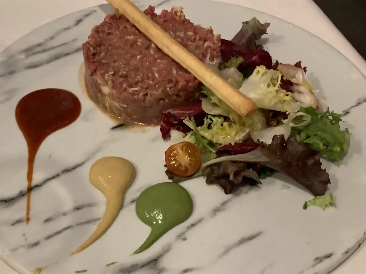 A steak tartare plated with a green salad and dotted sauces.