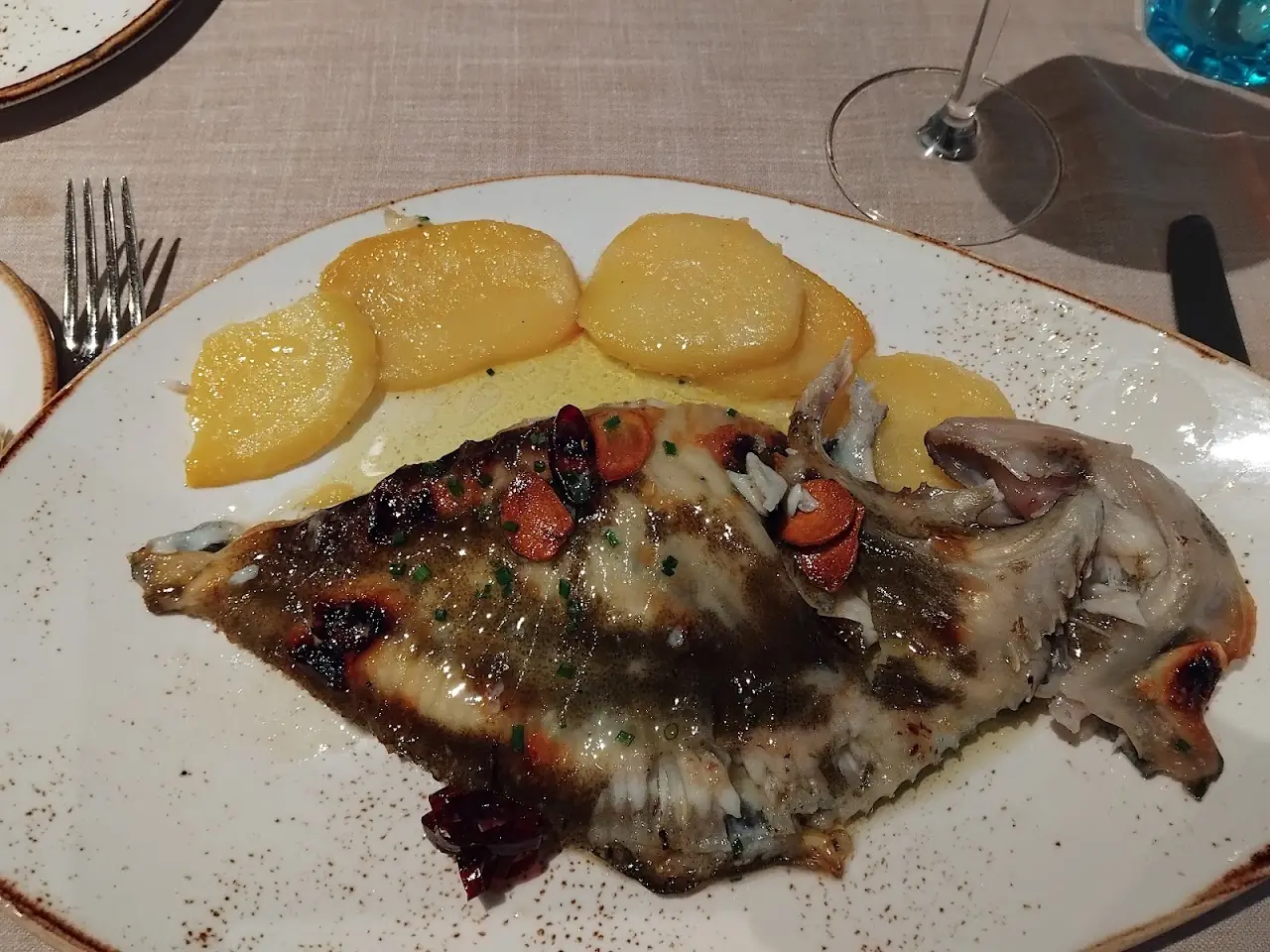 A whole grilled fish served with sliced potatoes.