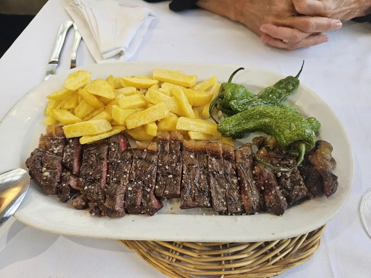 Sliced grilled steak with fries and green peppers on an oval plate