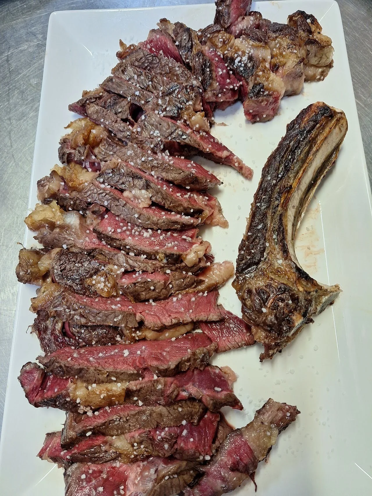 A platter of sliced grilled steak with a rib bone