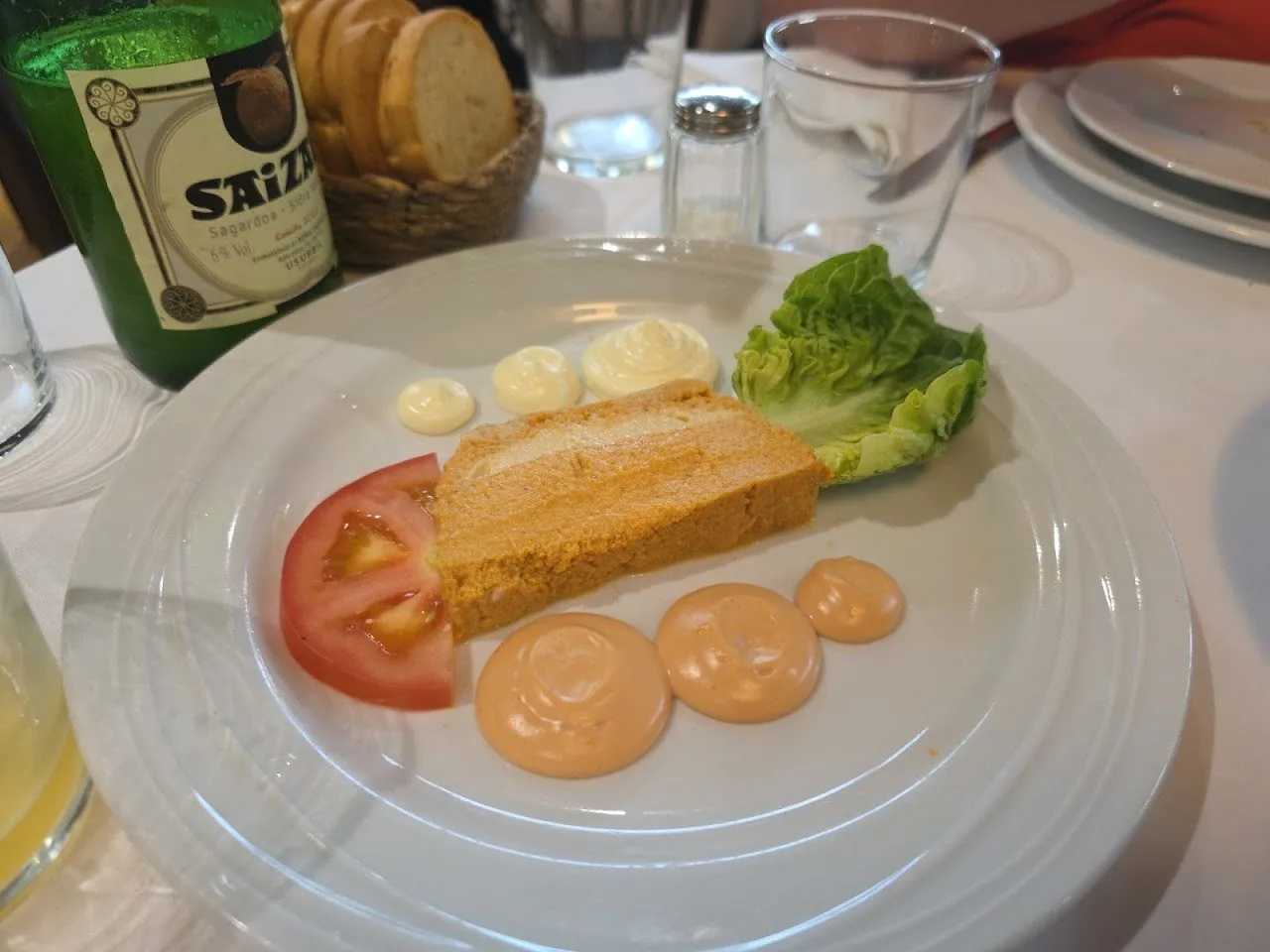 A slab of pale terrine with orange sauce and lettuce on a white plate