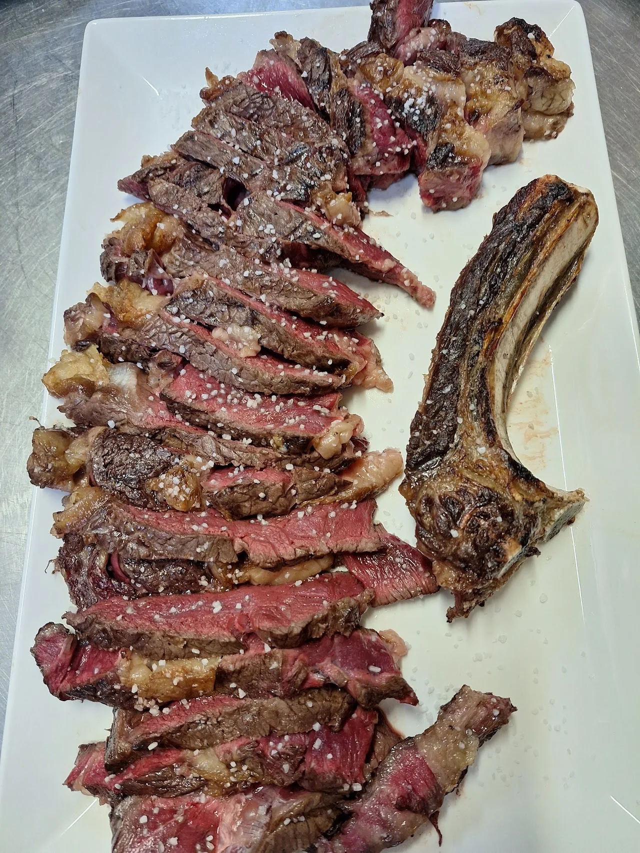 A sliced grilled steak fanned out on a white platter