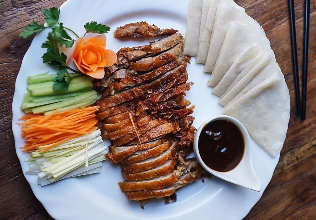 Sliced roast duck on a plate with pancakes, cucumber, carrot and dipping sauce