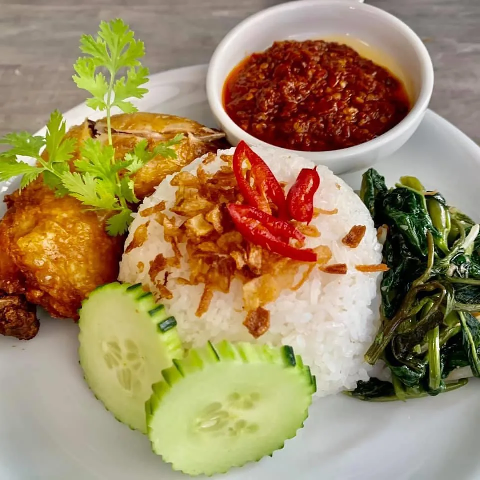 A plate of rice with satay skewers, fried egg-like fritters and chili sambal