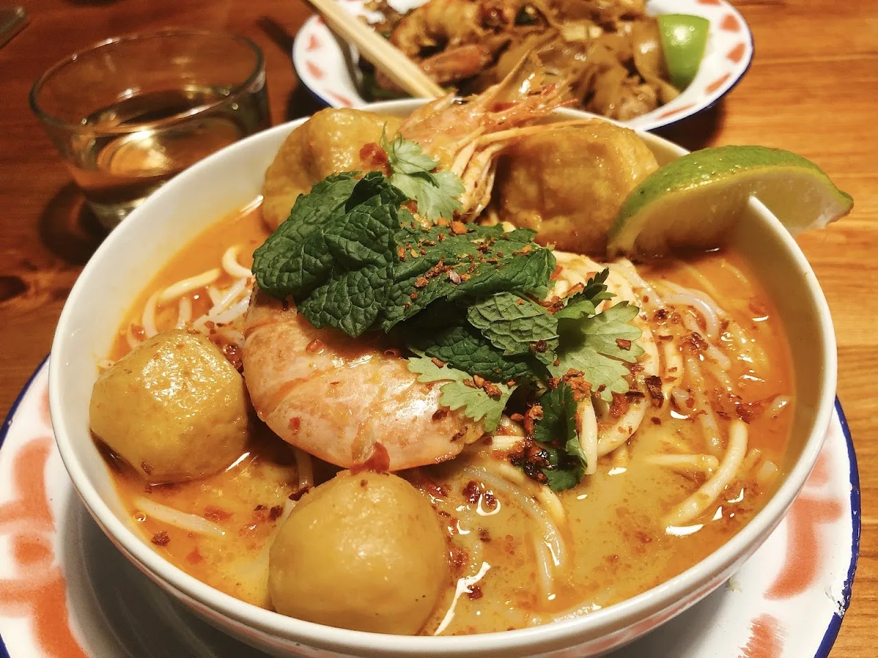 A bowl of noodle soup with dumplings, chicken and lime