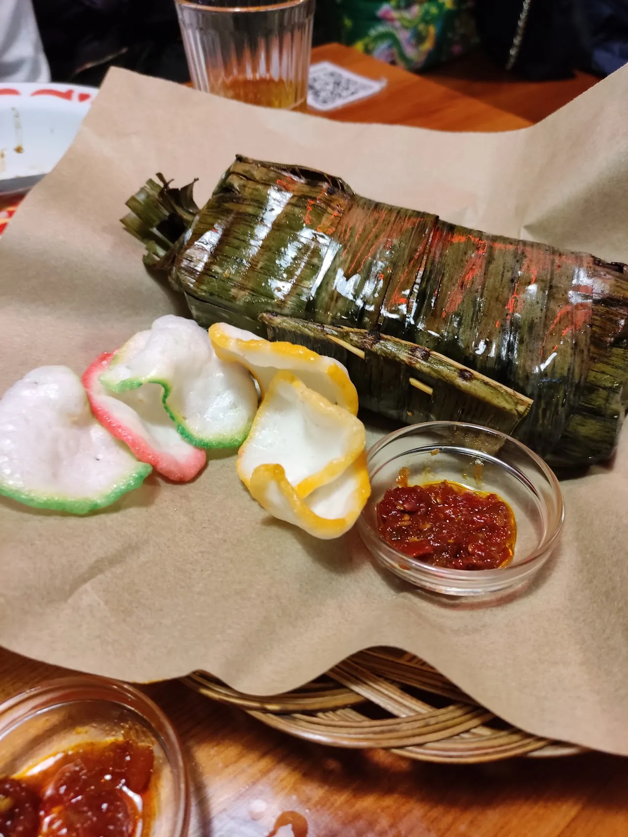 A grilled dish wrapped in banana leaf with pickled vegetable sides