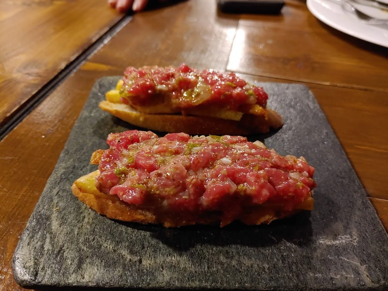 Two slices of toast topped with chopped red meat on a slate board