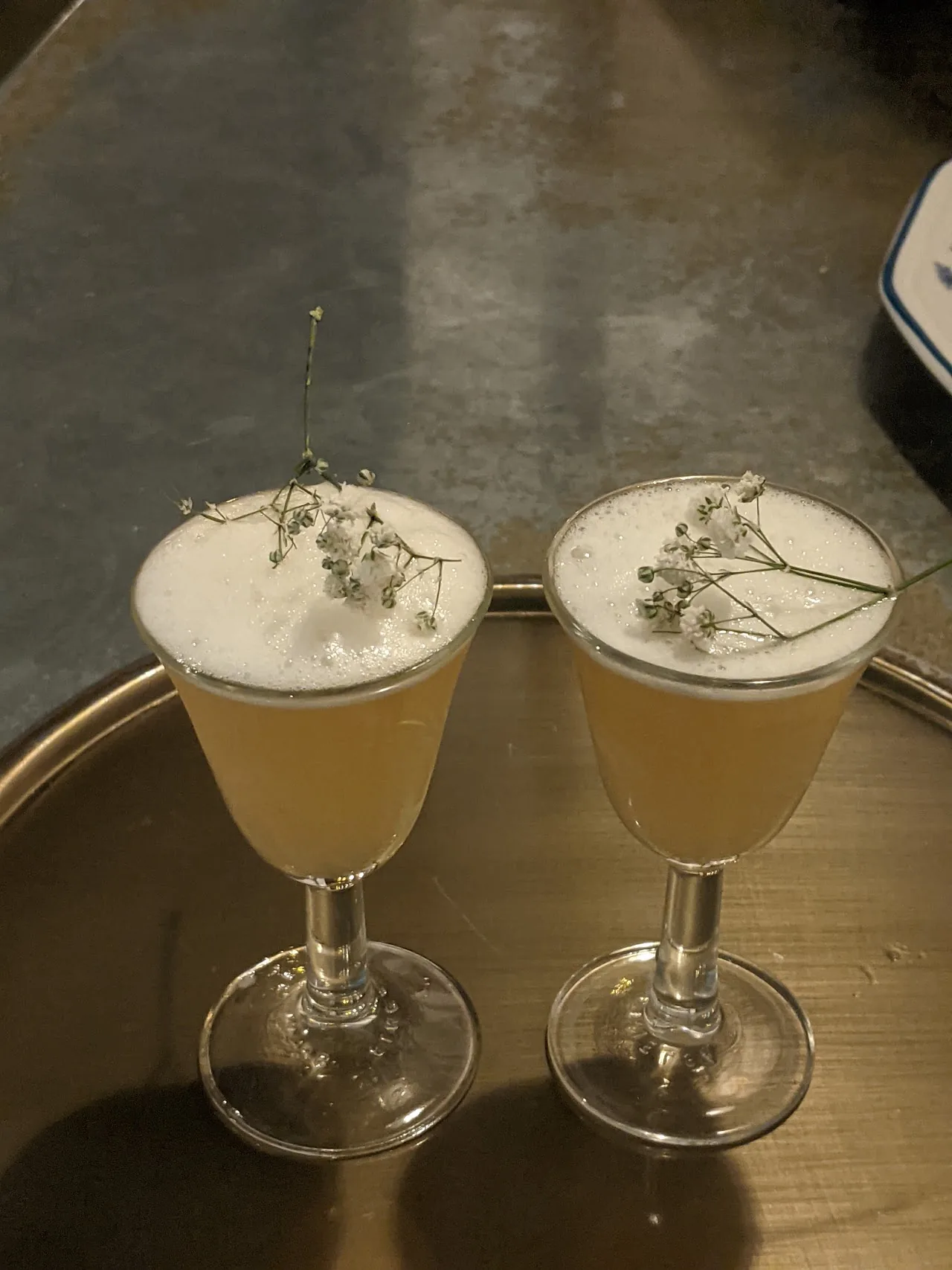 Two frothy yellow cocktails garnished with dried flowers