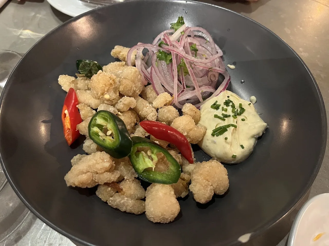 A bowl of fried squid rings with bell peppers, onion, and herb sauce