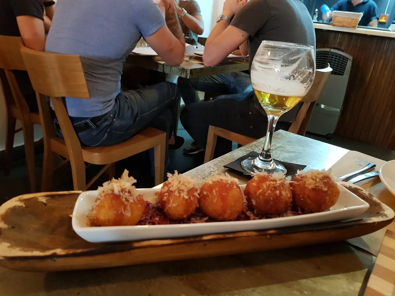 A wooden board of golden fried bites drizzled with red sauce, served with a beer