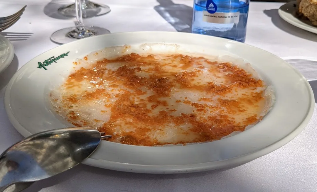 A white oval plate of baked fish topped with browned garlic breadcrumbs in a creamy sauce