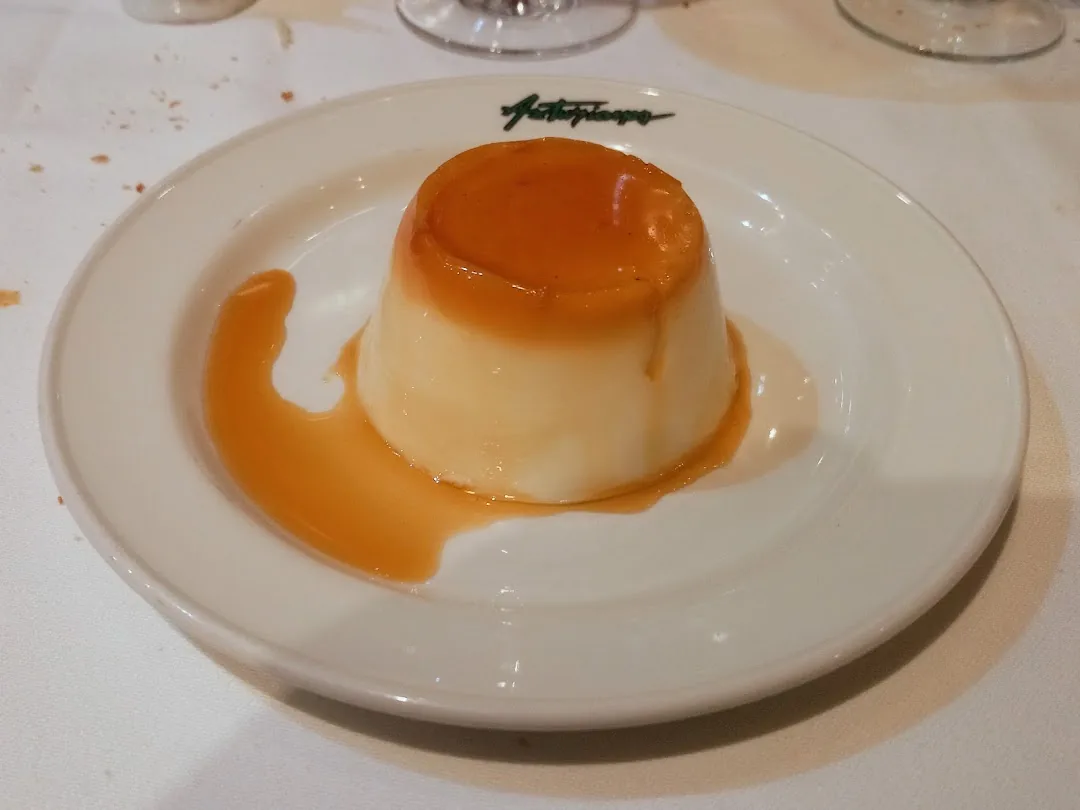 A caramel flan on a white plate with caramel sauce pooled around it