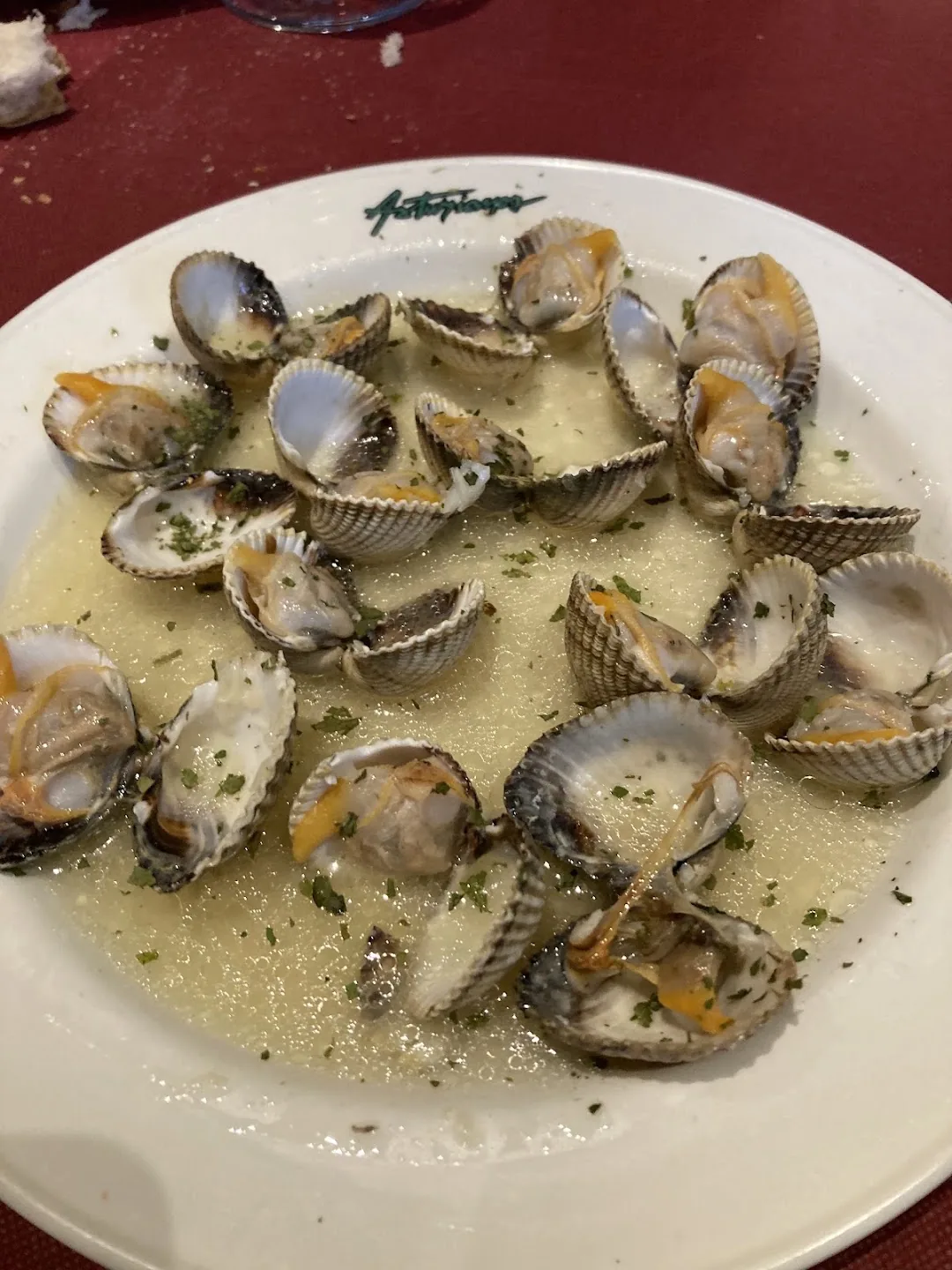 A white plate of open cockles in a garlic and parsley sauce