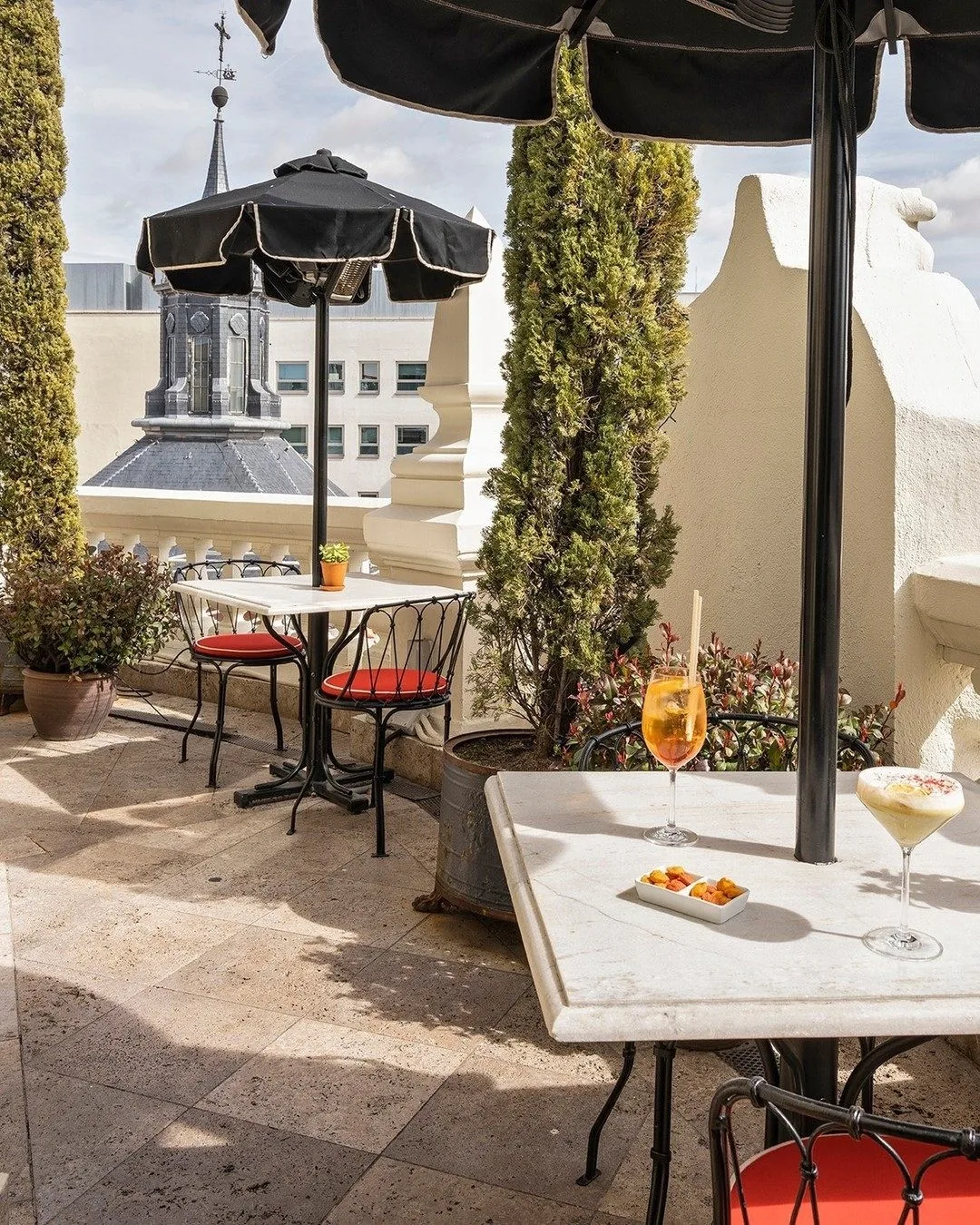 A sunny rooftop terrace with small tables and a drink