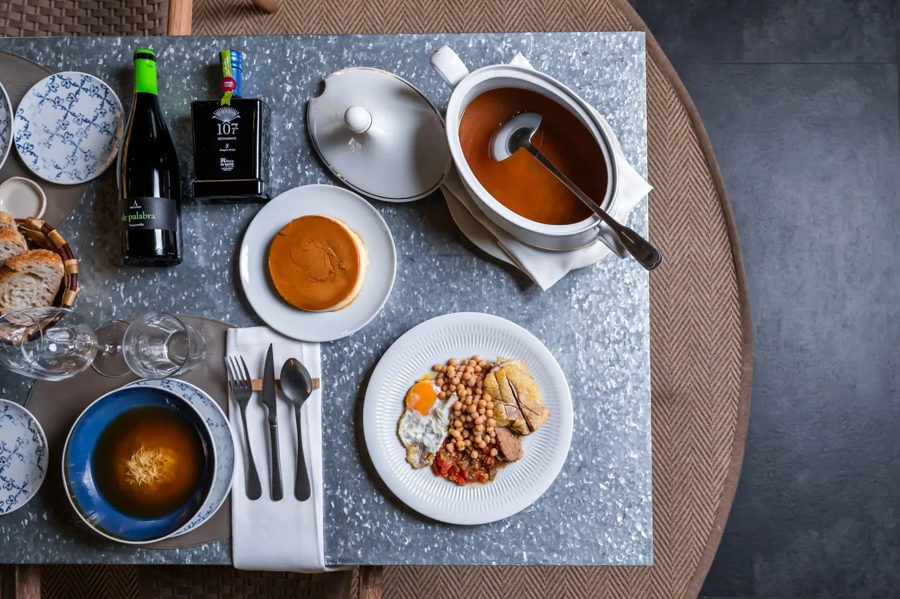 A table seen from above with a tureen of soup, a bowl of noodle soup, a flan and a plate of chickpeas with a fried egg