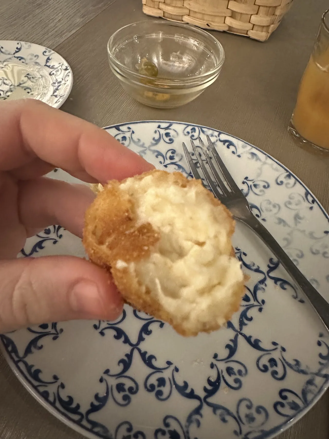 A hand holding a piece of golden baked bread on a patterned plate