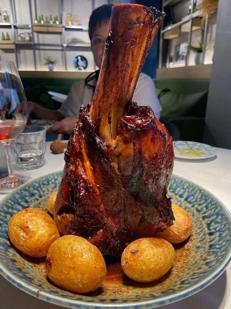 A braised lamb shank with roasted potato balls on a plate