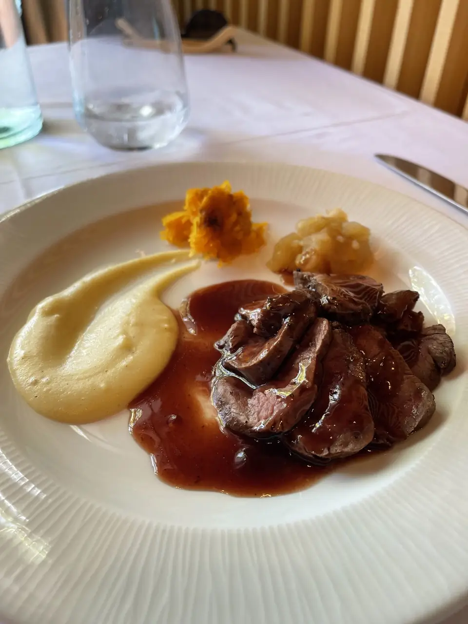 Sliced roasted meat in a red wine sauce with pureed sides and a small tomato relish