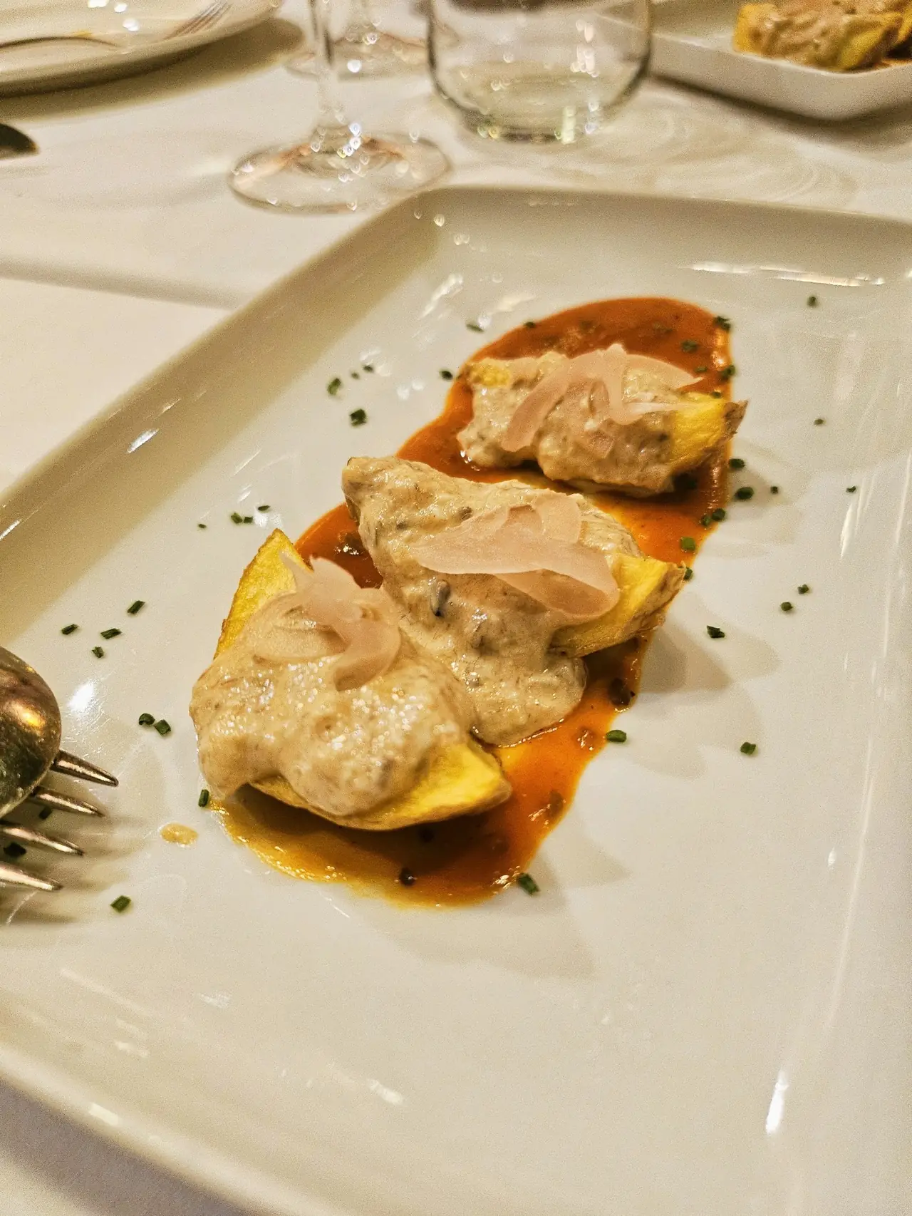 Fried potato slices topped with creamy sauce and shaved cured meat in a red sauce