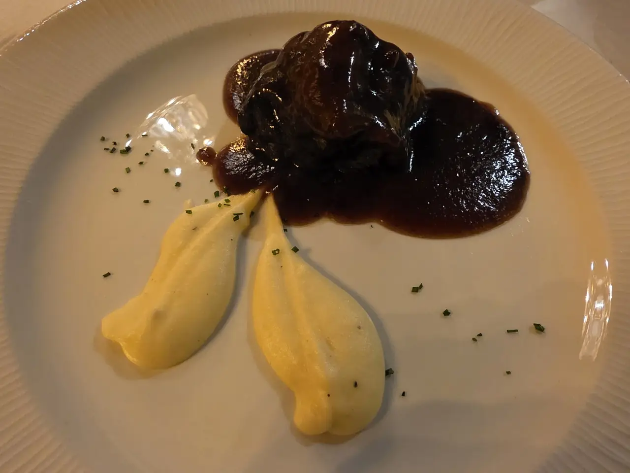 Braised meat in a dark reduction sauce with quenelles of mashed potato