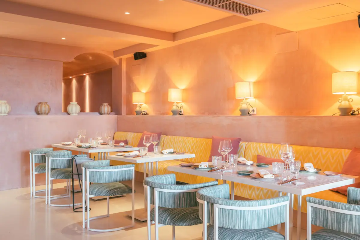 Warm terracotta-toned dining room with yellow ikat banquette, striped teal armchairs and shaded table lamps along a plastered ledge
