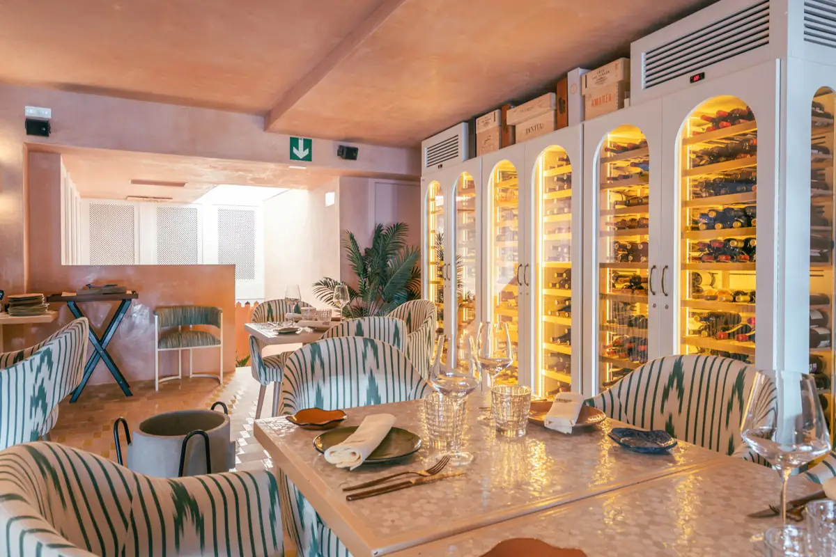 Dining room with illuminated arched wine cabinets full of bottles and green-striped upholstered chairs at set tables