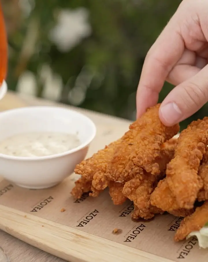 Basket of breaded fried chicken tenders next to a bowl of white dipping sauce