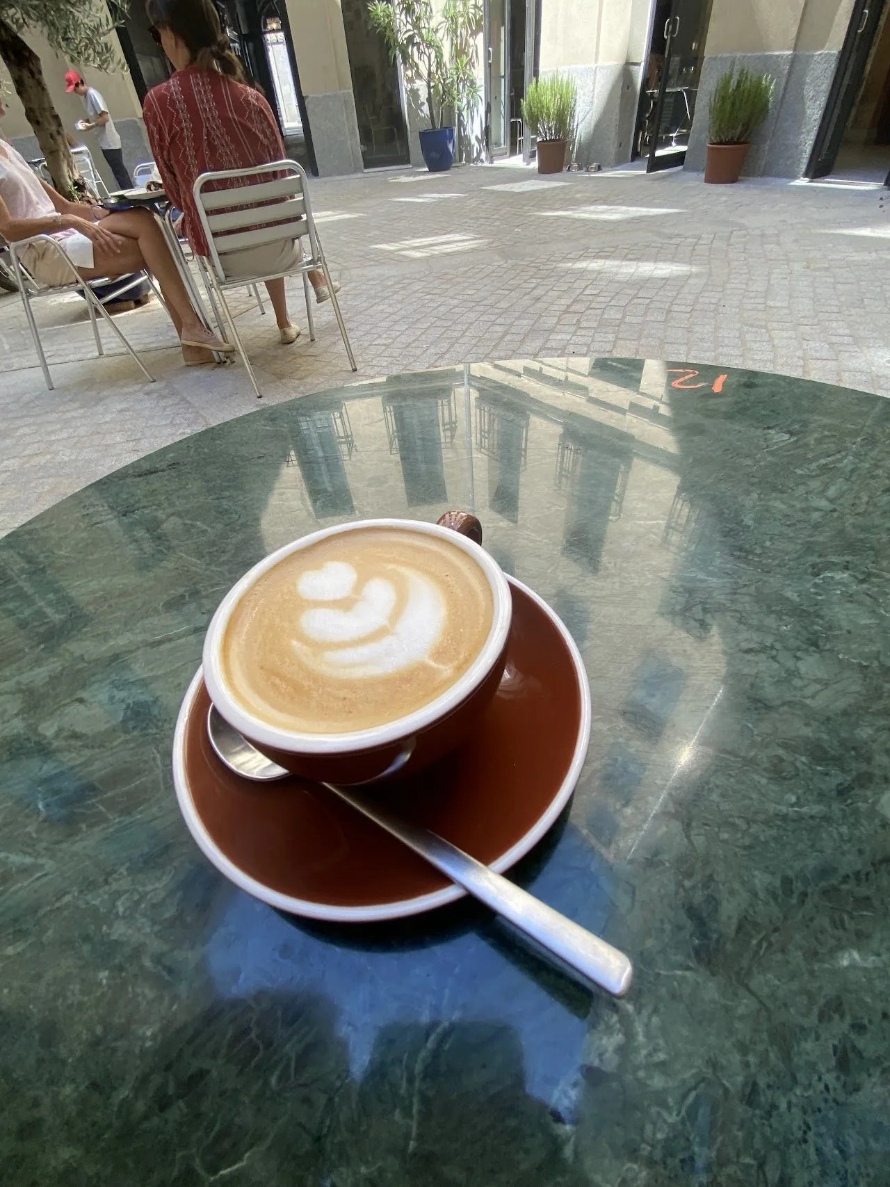 A latte with leaf-pattern art in a brown cup on a green marble table
