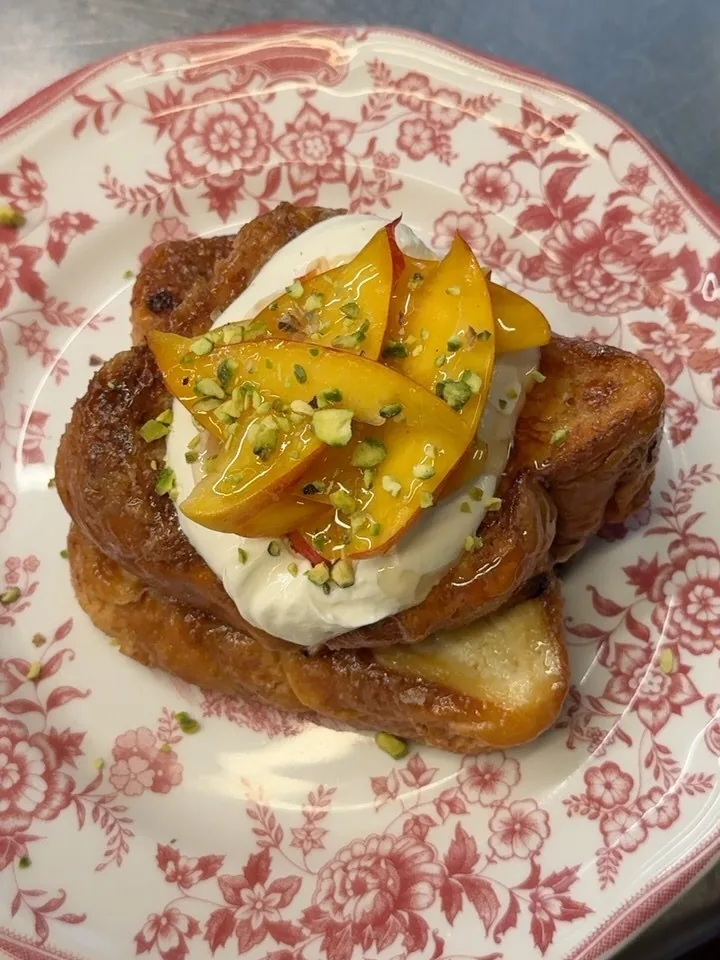 A slice of French toast topped with yogurt and yellow fruit on a floral-patterned plate