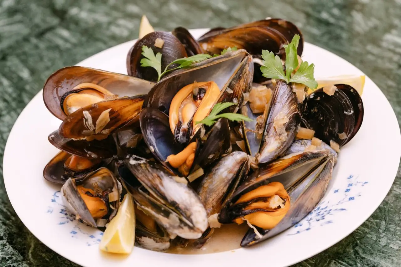 Plate of steamed mussels in broth garnished with parsley and lemon wedges on a floral-rimmed white plate