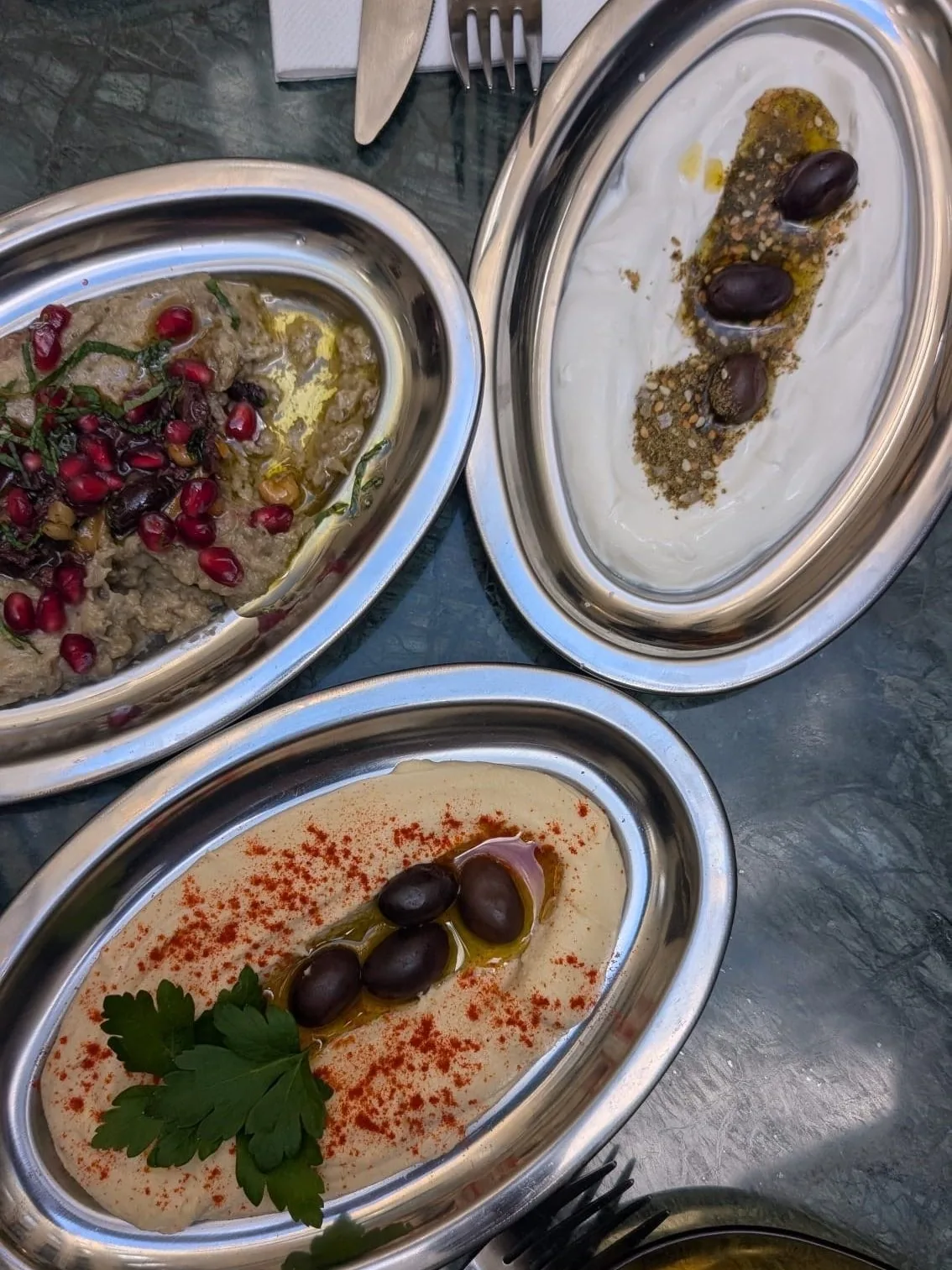Three small oval dishes of dips with olives and herbs on a marble table