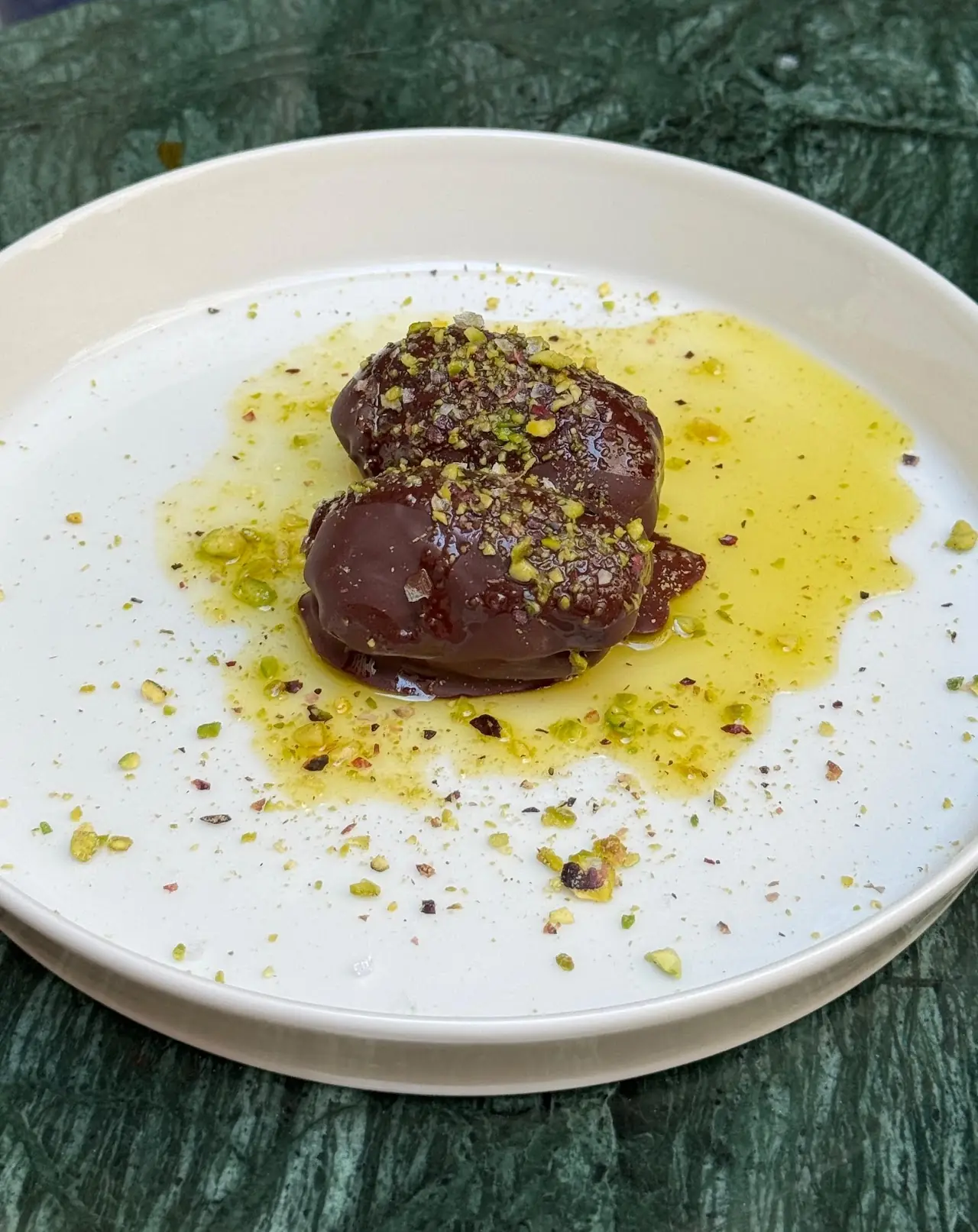 A round chocolate dessert drizzled with olive oil on a white plate.