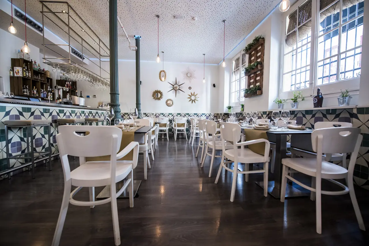 Dining room with a patterned green and purple tiled dado, sunburst mirrors on a white wall, white bentwood chairs and a bar along one side.