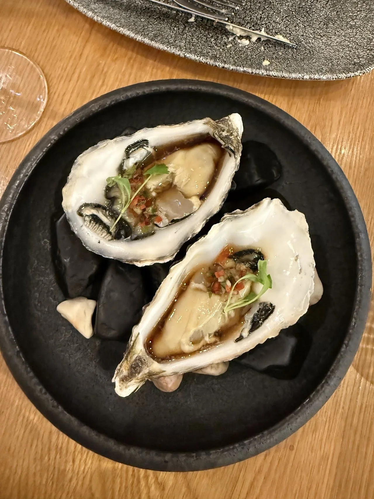 Two oysters with a garnish on a dark plate