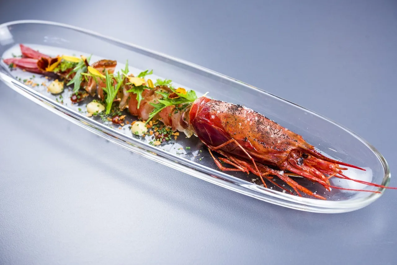 A red prawn laid on a long glass dish with a herb garnish