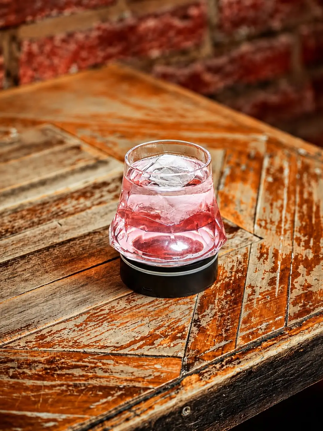 Pink cocktail with ice in a faceted glass on a weathered wooden table