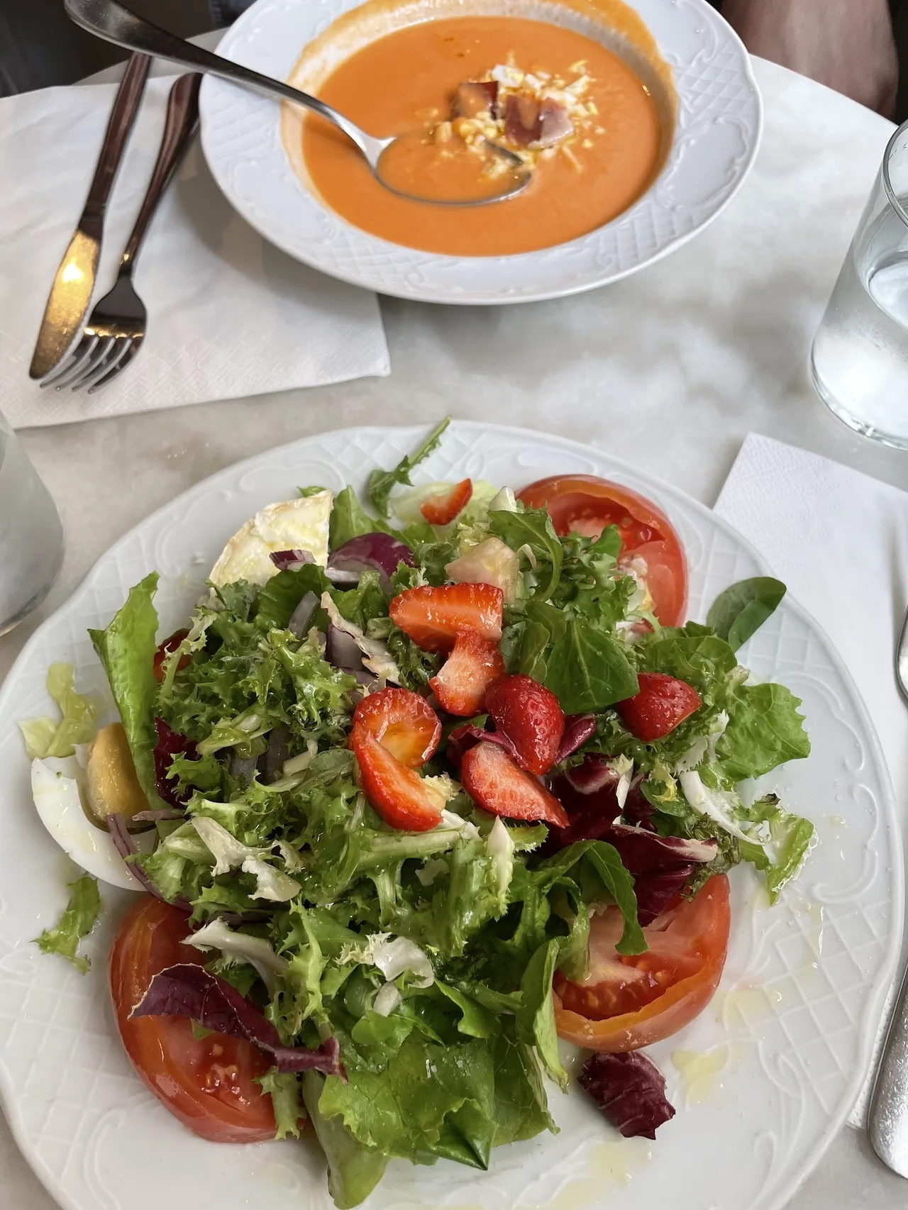 A white plate of mixed green salad with tomato slices and strawberries