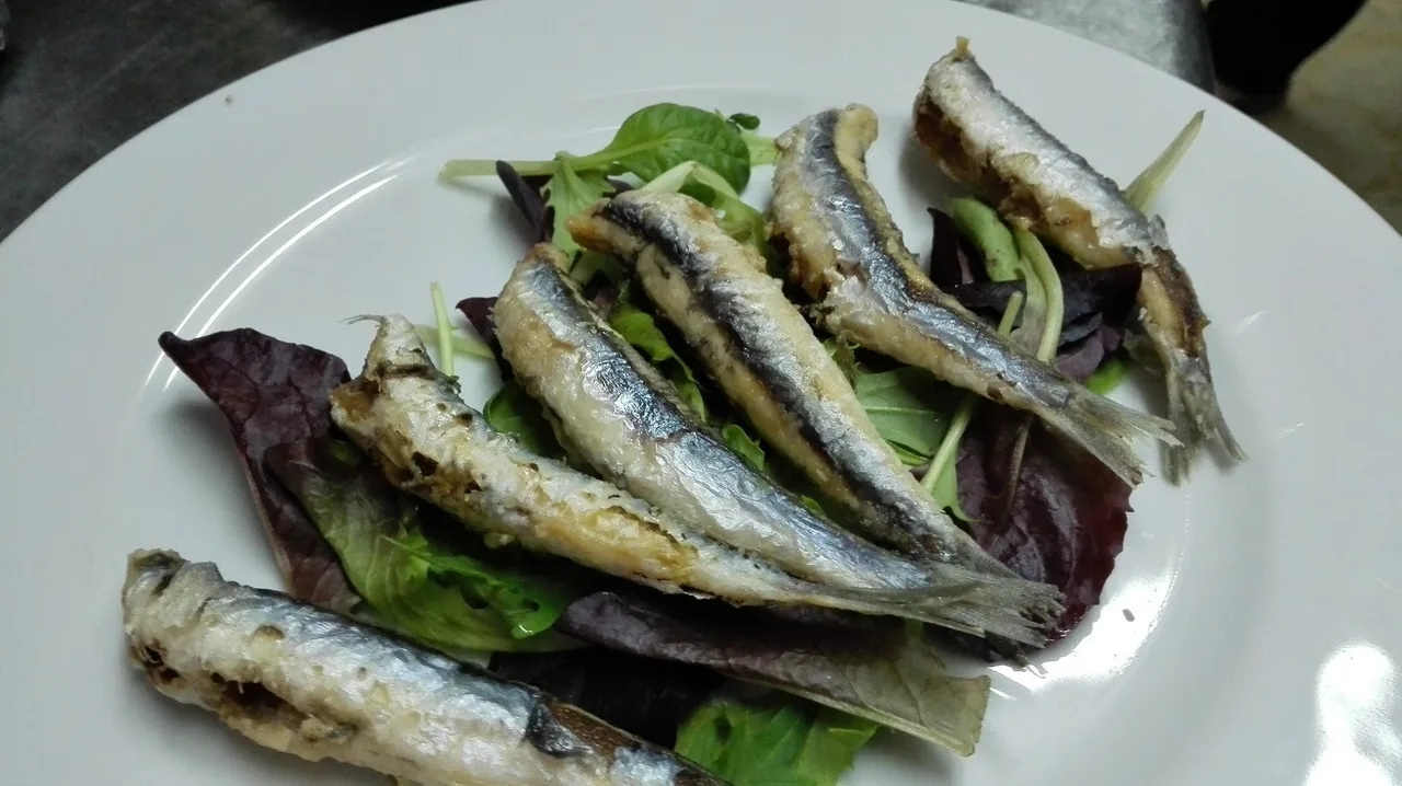 Small silvery fried fish on a bed of salad leaves on a white plate