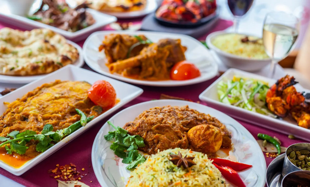 An overhead view of a table covered with plates of curries, rice, naan bread and grilled meats